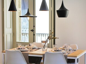 Una mesa de comedor dispuesta con platos, vasos y cubiertos, con tres lámparas colgantes arriba.