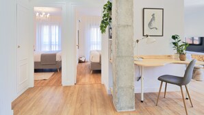 Un soggiorno moderno con pavimento in legno, un'imponente colonna in cemento, una scrivania con sedia e una televisione.