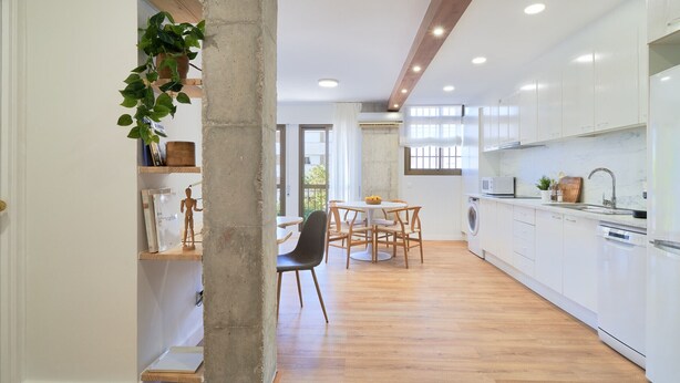Una cucina moderna con mobili bianchi, un'area pranzo con un tavolo rotondo e un grande pilastro in cemento.