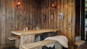 Une pièce rustique en bois, avec un banc, une table et des lampes fixées au mur.