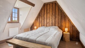 Une chambre avec un plafond en pente, des lambris en bois, un lit avec une literie blanche, des lampes de chevet et un banc en bois.
