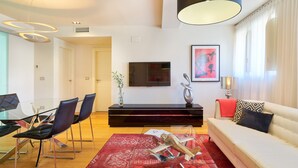 Un salon moderne avec une table basse en verre, un canapé, un coin repas avec des chaises et un téléviseur fixé au mur.