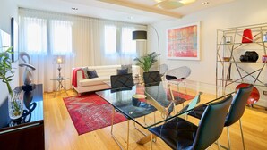 Un salon moderne avec une table à manger en verre, des chaises noires, un canapé blanc et un tapis rouge.