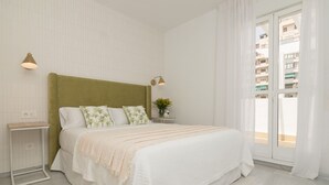 A bedroom with a bed, nightstands, a window with curtains, and a view of buildings outside. - Top-Floor Apartment Elegance in Carihuela, Torremolinos with Pool and Terrace (Torremolinos)