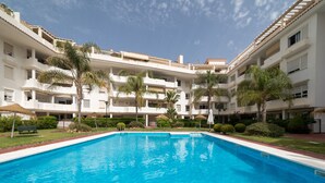 A swimming pool surrounded by a multi-story building with balconies, palm trees, and a clear sky. - Top-Floor Apartment Elegance in Carihuela, Torremolinos with Pool and Terrace (Torremolinos)