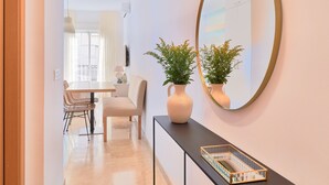 A modern interior with a dining area, a console table with a vase and a mirror, and a view into a room with a balcony. - Charming Studio with French Balcony in Upper Málaga, Close to Downtown (Málaga)