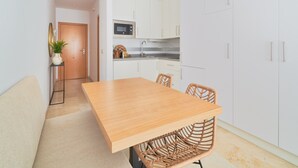 A modern kitchen with white cabinets, a wooden dining table, and wicker chairs. - Charming Studio with French Balcony in Upper Málaga, Close to Downtown (Málaga)