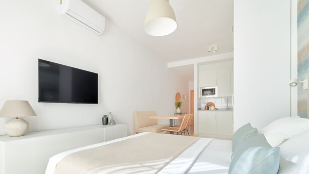 A modern bedroom with a bed, bedside table, lamp, and a TV on the wall. - Charming Studio with French Balcony in Upper Málaga, Close to Downtown (Málaga)