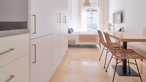 A modern kitchen with white cabinets and a dining area with a wooden table and wicker chairs. - Charming Studio with French Balcony in Upper Málaga, Close to Downtown (Málaga)