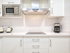 Une cuisine moderne avec des meubles blancs, un four à micro-ondes encastré, une machine à café et un grille-pain.