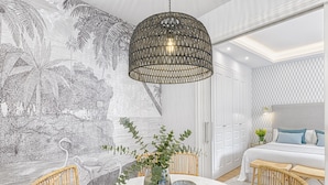 Ett sovrum med en stor säng, en hängande lampa, en väggmålning och möbler i rotting.