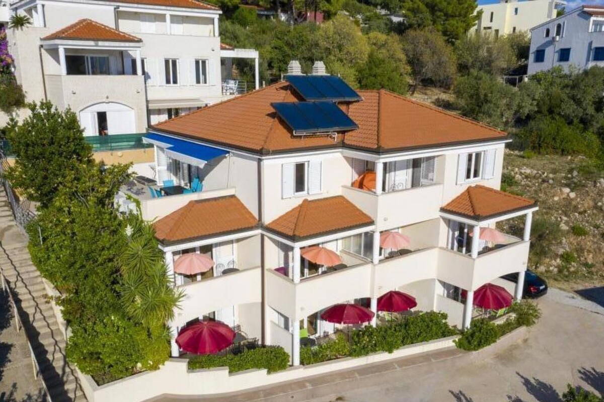 Un edificio de varios pisos con balcones, paneles solares y mesas exteriores con sombrillas.