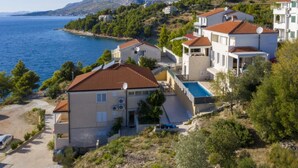 A coastal residential area with houses featuring red-tiled roofs, a swimming pool, and a view of the sea and mountains. - Apartments Radevenjić (Omis)