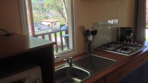 A compact kitchen with a sink, stove, and window overlooking a deck. - Mobile home with terrace - 4 guests (Saint-Girons)