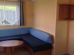 A small room with a blue sofa, a round wooden table, and a window with curtains. - Mobile home with terrace - 4 guests (Saint-Girons)