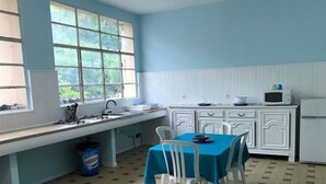 Een keuken met een raam, witte kasten, een spoelbak, een fornuis, een magnetron en een tafel met stoelen.
