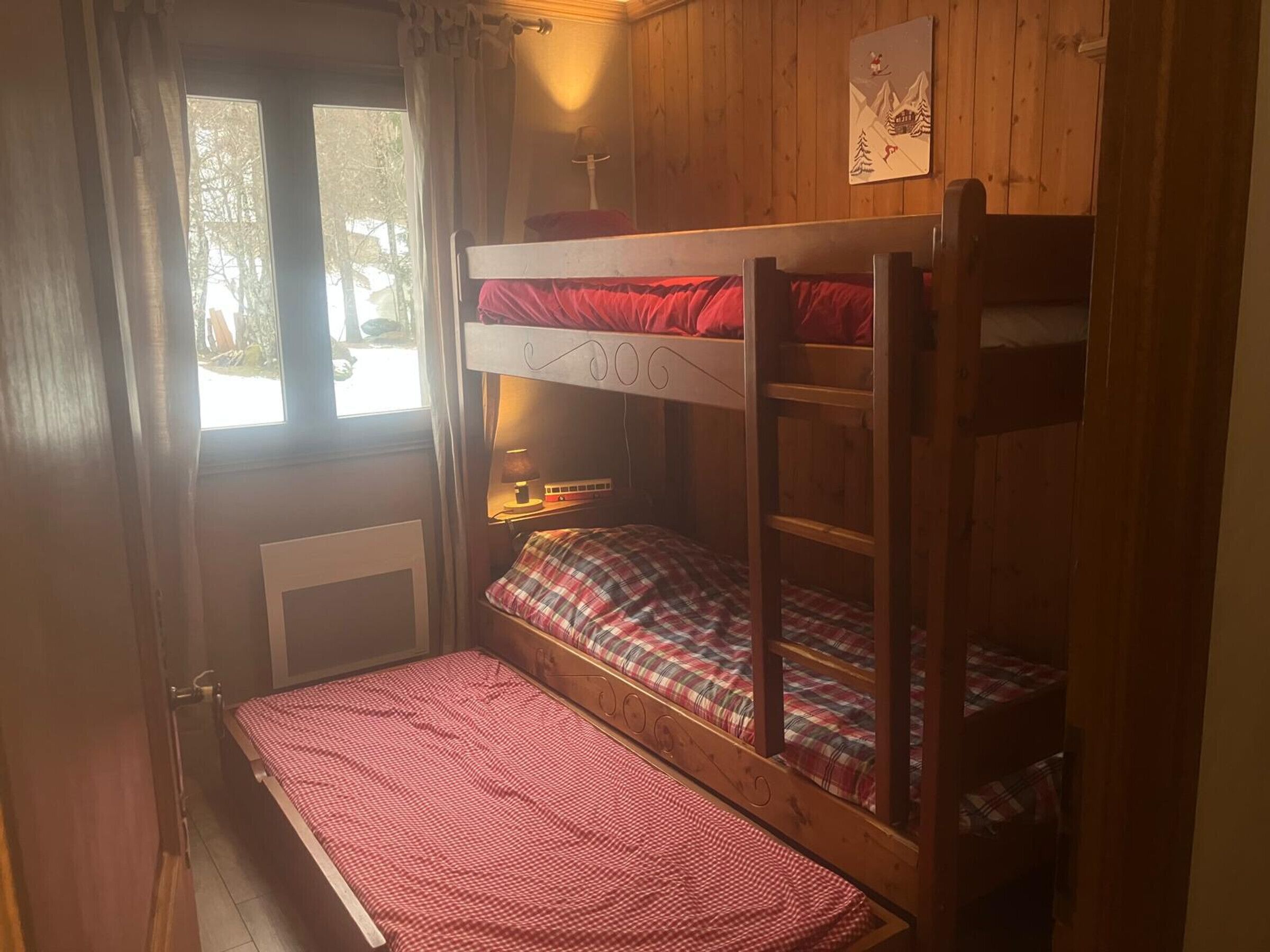 Quarto com beliche, janela, pequena mesa com luminária e um quadro na parede.
