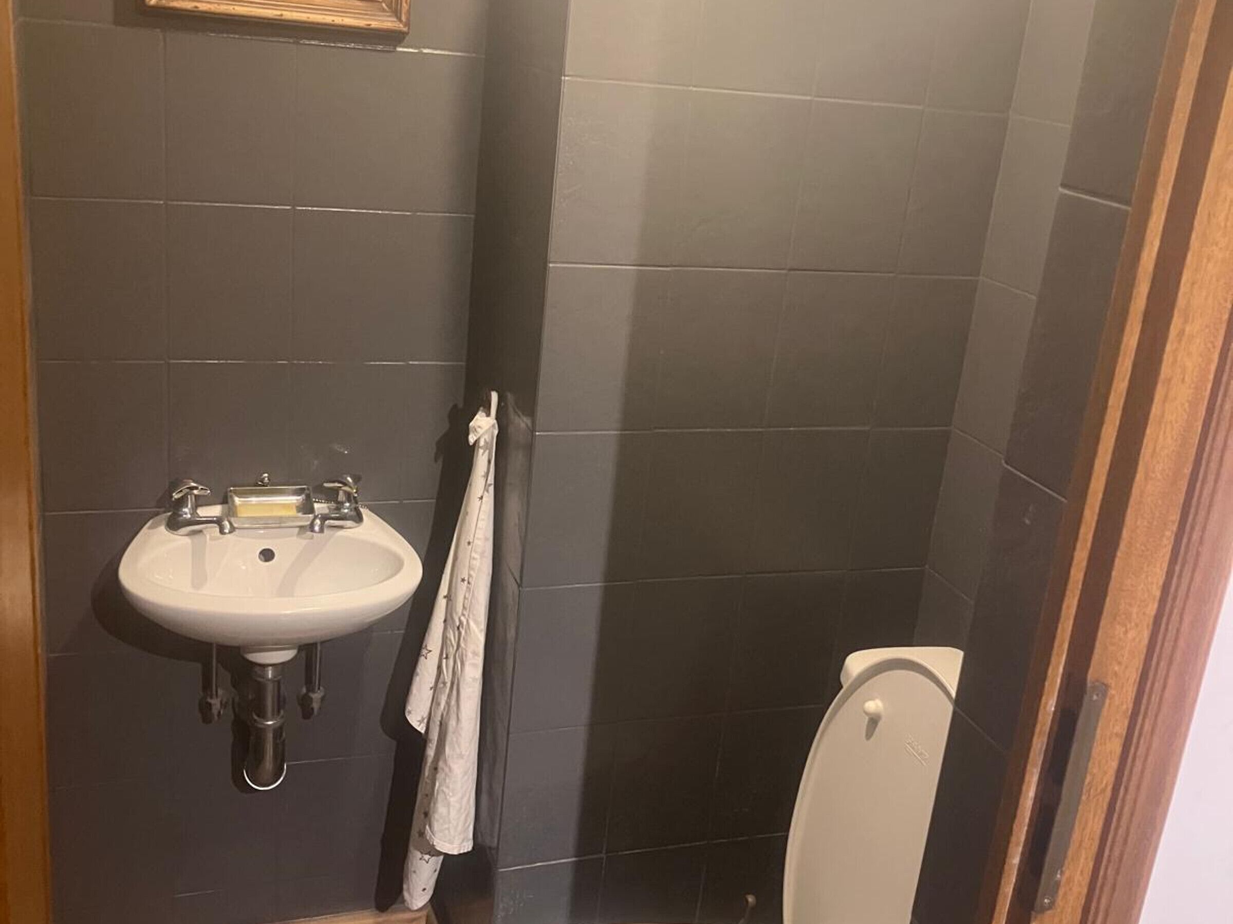 A bathroom with a white sink, dark tiles, and a toilet.