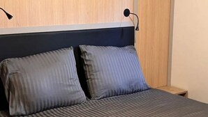 Un lit avec une couvre-lit à rayures et deux oreillers, une tête de lit en bois et une table de chevet avec une lampe.