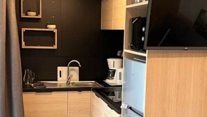 Une cuisine compacte dotée d’armoires en bois, d’un plan de travail noir, d’un évier en acier inoxydable, d’un four à micro-ondes, d’une machine à café et d’un réfrigérateur.