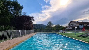 Une piscine rectangulaire à l’eau d’un bleu limpide, entourée d’une clôture blanche et d’une zone herbeuse.