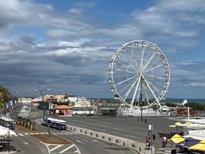 Ein großes Riesenrad, eine Straßenbahnlinie und ein Ufergebiet mit Gebäuden und Geschäften.