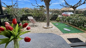 Une terrasse avec une table, une chaise, un arbre et une petite pelouse.
