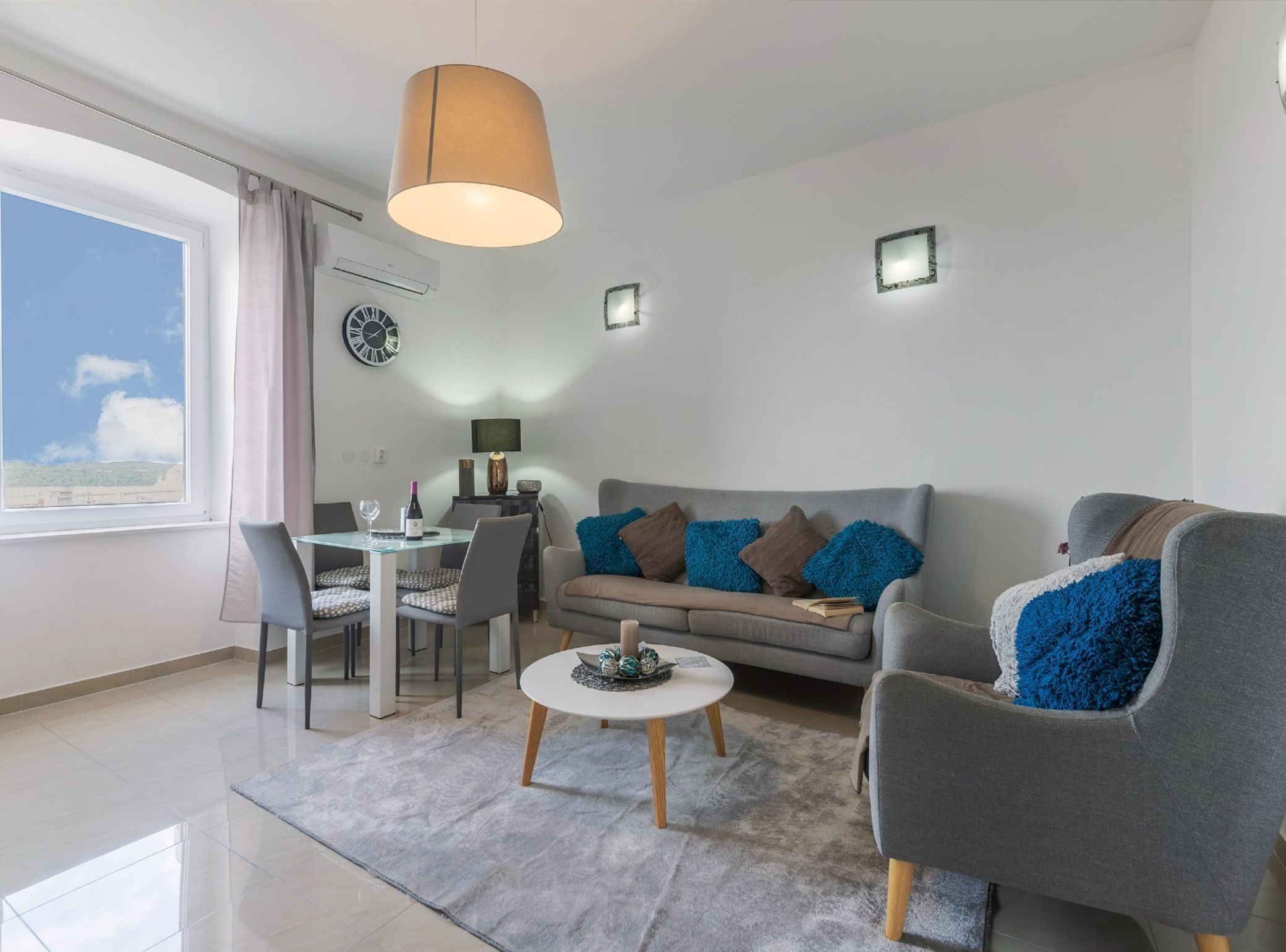 A modern living room with a grey sofa, a round coffee table, and a dining area with a glass table and chairs.