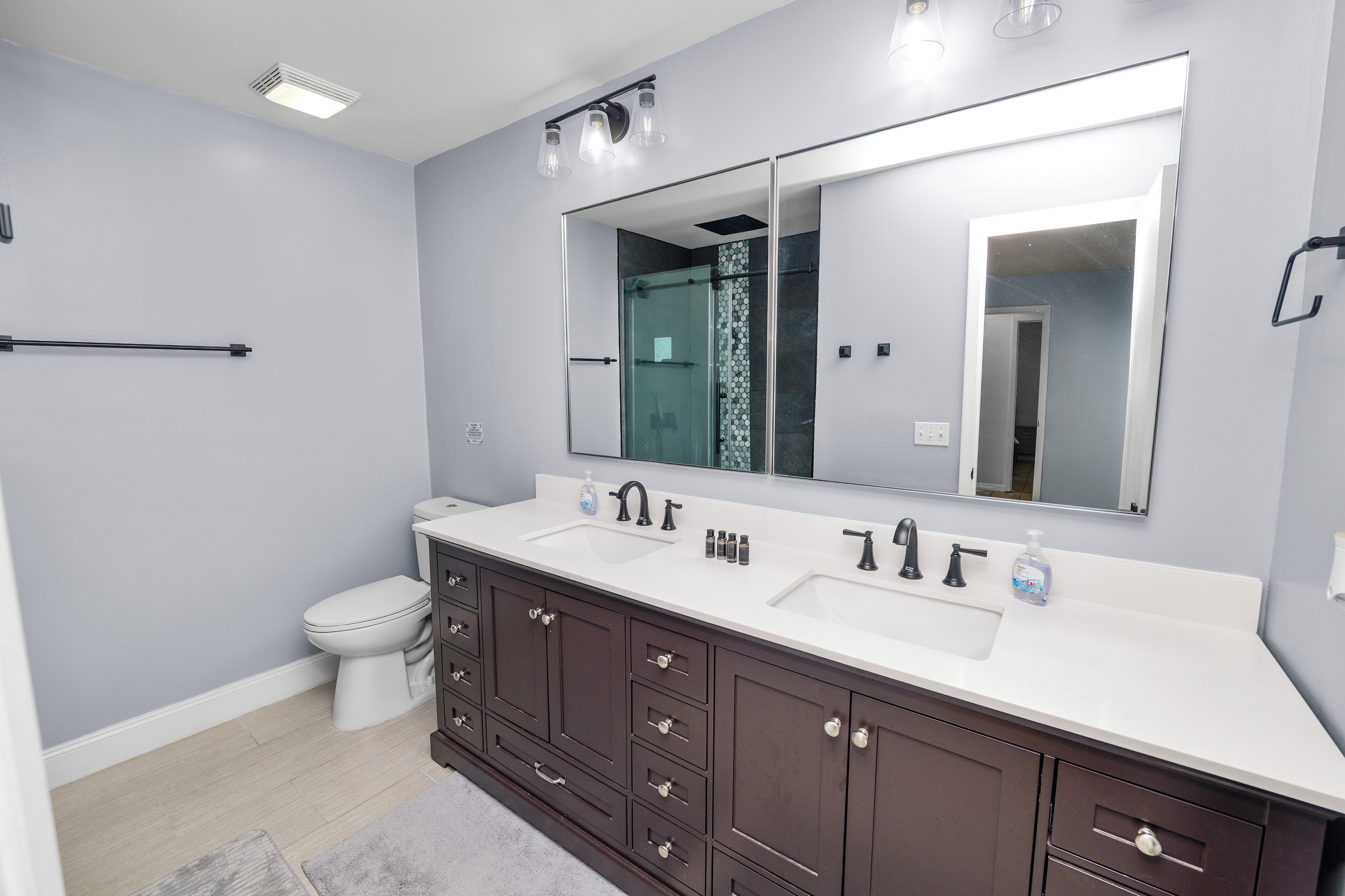 A modern bathroom with a large mirror, two sinks, a toilet, and dark wooden cabinets.