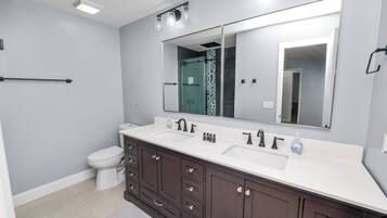 A modern bathroom with a large mirror, two sinks, a toilet, and dark wooden cabinets.