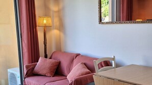 Een kamer met een houten tafel, een rode bank met een plaid, een vloerlamp en een spiegel aan de muur.