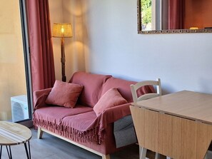 A room with a wooden table, a red sofa with a throw blanket, a floor lamp, and a mirror on the wall. - Cozy Studio with Terrace in Mèze - Private Parking (Mèze)
