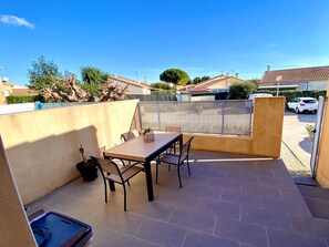 Une terrasse avec une table et des chaises, une plante en pot et une voiture garée au fond.