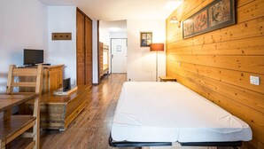 Um quarto com piso de madeira, uma cama, uma escrivaninha com computador e uma luminária.
