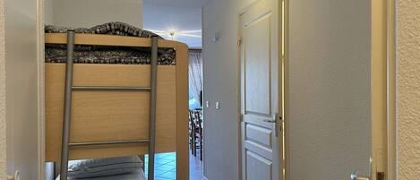 A narrow hallway with a bunk bed on the left and a closed door on the right.