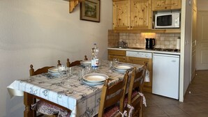 A dining area with a table set for four, wooden cabinets, a microwave, and a dishwasher. - Cozy Apartment for 4 with Balcony and Parking in Montgenèvre (Montgenèvre)