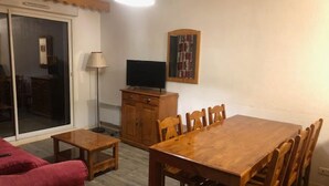 Un coin repas avec une table et des chaises en bois, un téléviseur posé sur un meuble, et un canapé rouge.