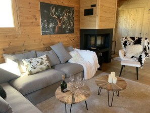 A cozy cabin interior with a wooden log wall, a fireplace, a sofa, a chair, and a table with candles. - Cozy Chalet in Montgenèvre with WIFI and Fireplace (Montgenèvre)