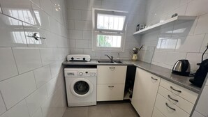 A compact kitchen with white tiles, a washing machine, a sink, and a window. - Spacious apartment 5 min from beach, 2 bedrooms, terrace, parking, WIFI (Roses)