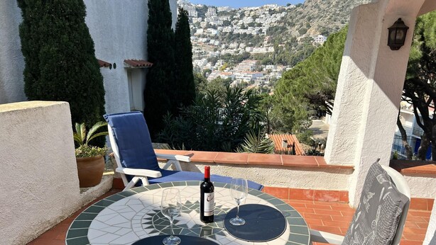 A round table with a mosaic design, two blue cushioned chairs, a bottle of wine, and two wine glasses. - Spacious apartment 5 min from beach, 2 bedrooms, terrace, parking, WIFI (Roses)