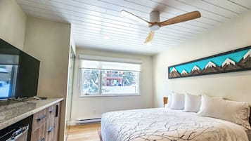 A bedroom with a bed, a ceiling fan, a window with a view, and a mounted artwork.