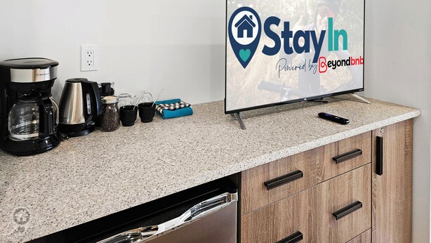 A kitchen counter with a coffee maker, cups, and a TV displaying 'StayIn Powered by Beyondbnb'. - Renovated hotel-style room at Toby Creek (Panorama)