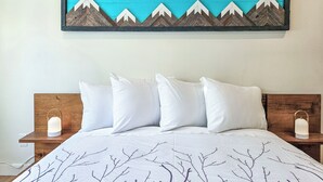 A neatly made bed with white bedding and a mountain-themed artwork above it. - Renovated hotel-style room at Toby Creek (Panorama)