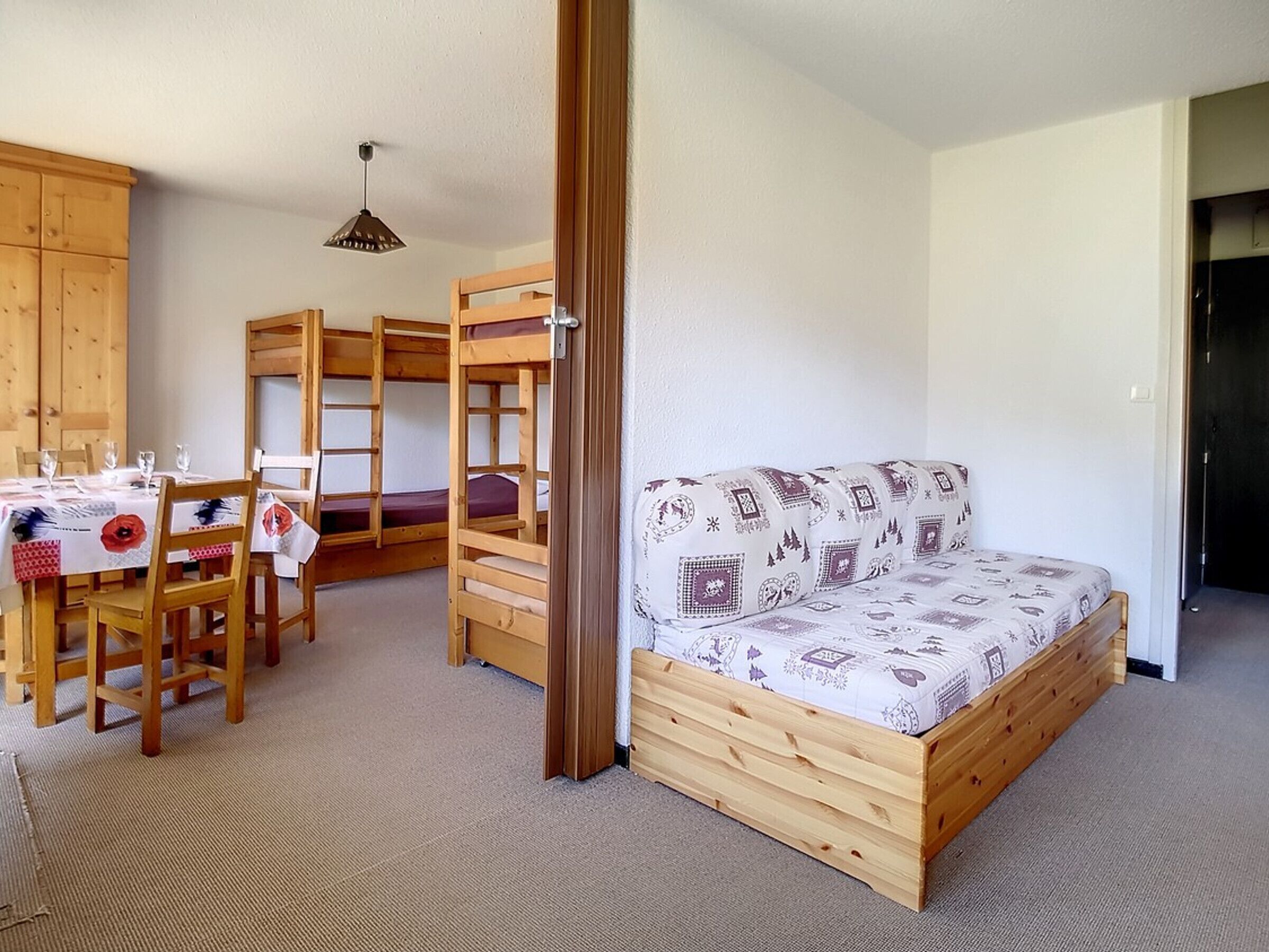 A room with bunk beds, a sofa, a dining table with chairs, and a hanging light fixture.