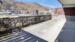 A balcony with a stone wall, a view of a mountainous landscape, and buildings in the background. - Bright Apartment · Ski-in/Ski-out · Terrace & Ski Locker (Les Menuires)