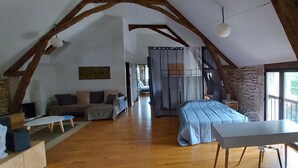 Ruime loft slaapkamer met een stenen muur, houten balken, een bed, een bureau en uitzicht op het groen.