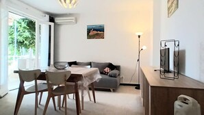 Uma área de refeições com mesa, cadeiras, sofá, luminária de chão e um rack com televisão.