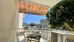 Uma varanda com mesa e cadeiras, com vista para uma área residencial com palmeiras e um edifício ao fundo.