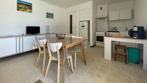 Uma cozinha compacta com área de jantar, armários brancos, uma TV e uma cafeteira.
