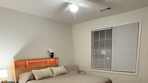 Un dormitorio con cama de madera, mesita de noche, ventilador de techo y ventana con persianas.
